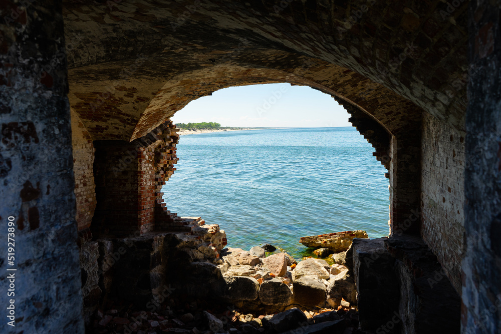 The arch of the Western Fort, located on the seashore. A seascape of blue sea waves through a red brick arch, a view from an old brick fort on the seashore. Ruins of an old fortress on the seashore. 