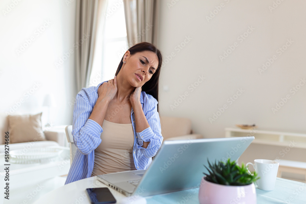 Businesswoman feeling pain in neck after sitting at the table with laptop. Tired female suffering of office syndrome because of long hours computer work. Pretty girl massaging her tense neck muscles Businesswoman feeling pain in neck after sitting at the table with laptop. Tired female suffering of office syndrome because of long hours computer work. Pretty girl massaging her tense neck muscles