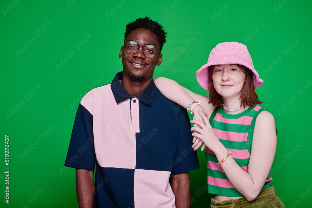 Obraz premium Portrait of stylish multiethnic teenage couple in fashion clothes smiling at camera posing against green background