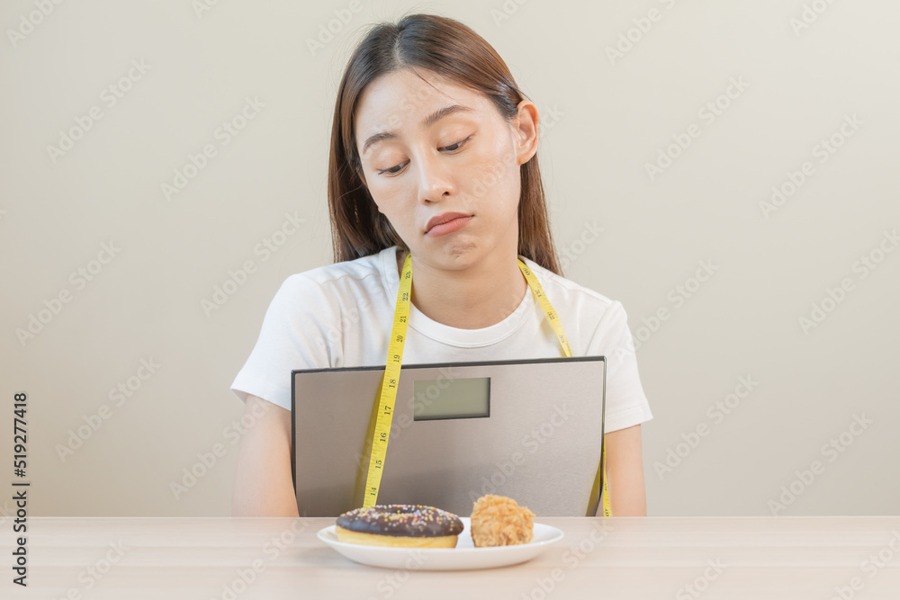 Diet, attractive asian young woman, girl restrained to eat doughnut, bakery and fried chicken, fast food to lose, loss weight, hugging weight scales on table at home. Passion, temptation when hungry. Diet, attractive asian young woman, girl restrained to eat doughnut, bakery and fried chicken, fast food to lose, loss weight, hugging weight scales on table at home. Passion, temptation when hungry.