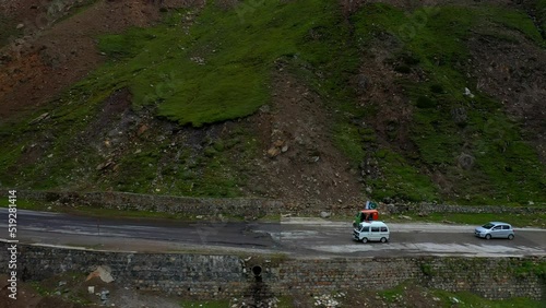 Drone shot of a Tuk Tuk on the Babusar Pass mountain pass in Pakistan, with a few vehicles on the road in the Kaghan Valley, wide panning shot photo