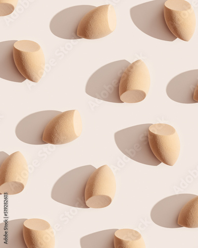 Minimal pattern from makeup sponges for foundation cream on beige color background with dark shadows. Beauty blender egg shape. Aesthetic flat lay cosmetic sponge, top view graphic layout © yrabota