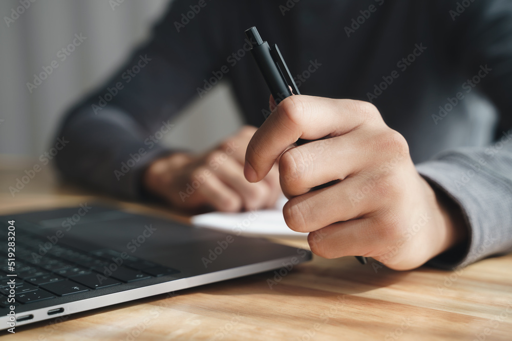 businessman holding pen by left hand working with laptop at office. businessman holding pen by left hand working with laptop at office.