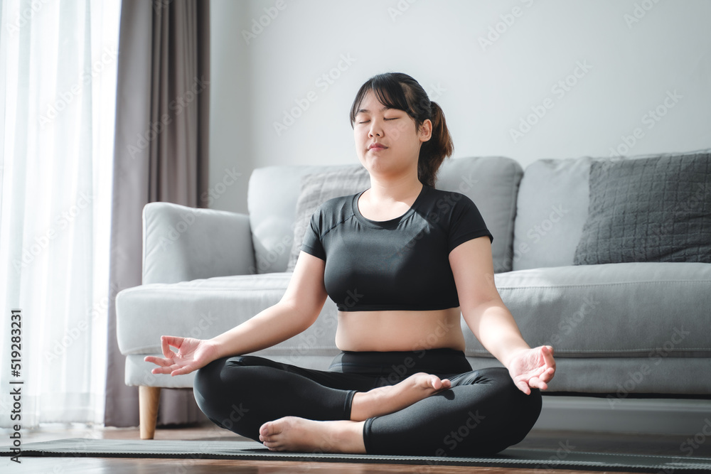 Asian chubby woman sitting on the floor in living room practice yoga lesson. female having meditate training class..
