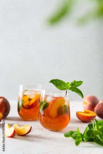 Fresh Peach iced tea. Iced tea with peach slices, mint and ice cubes on a white background. Copy space for text. Homemade refreshing summer drink recipe. Refreshing peach lemonade. Summer cold drink
