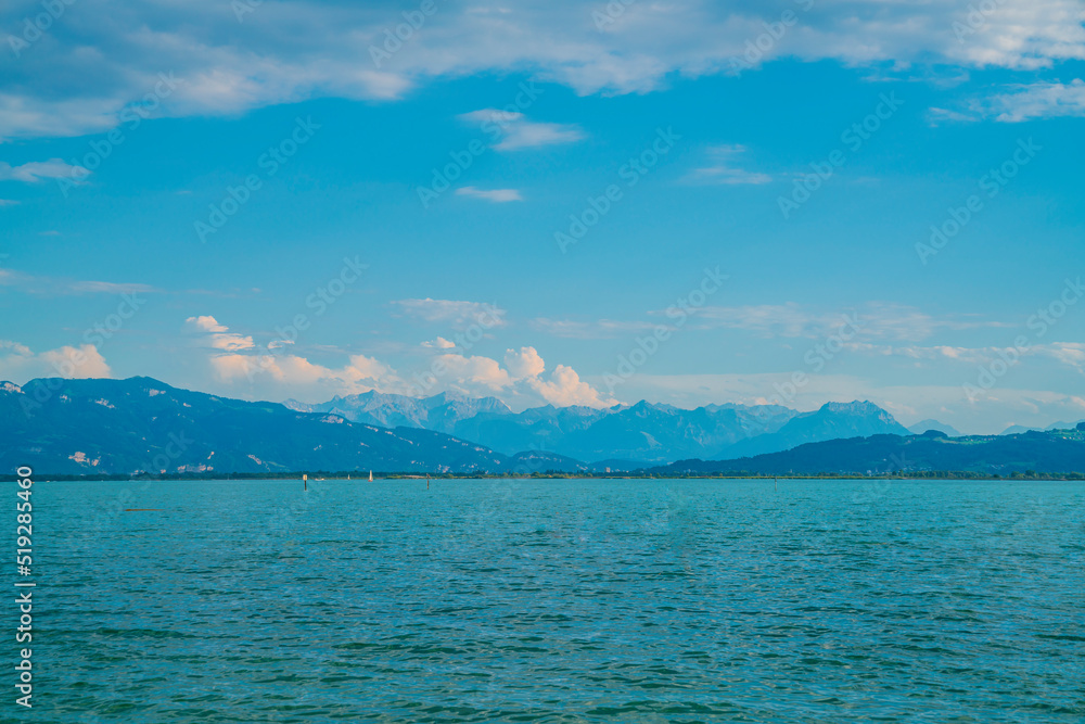 Germany, Beautiful bodensee panorama landscape view to snow covered mountain peaks of alps nature from water with sailboats in summer at sunset