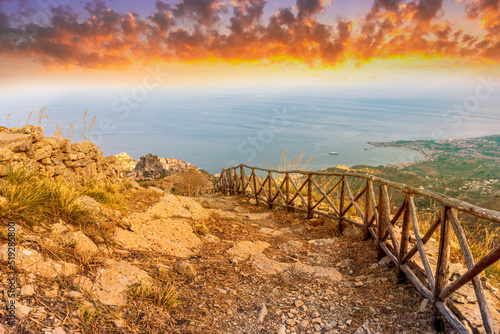 mountain landscape with a hiking trail leading to a mountain town and beautiful blue seashore far away