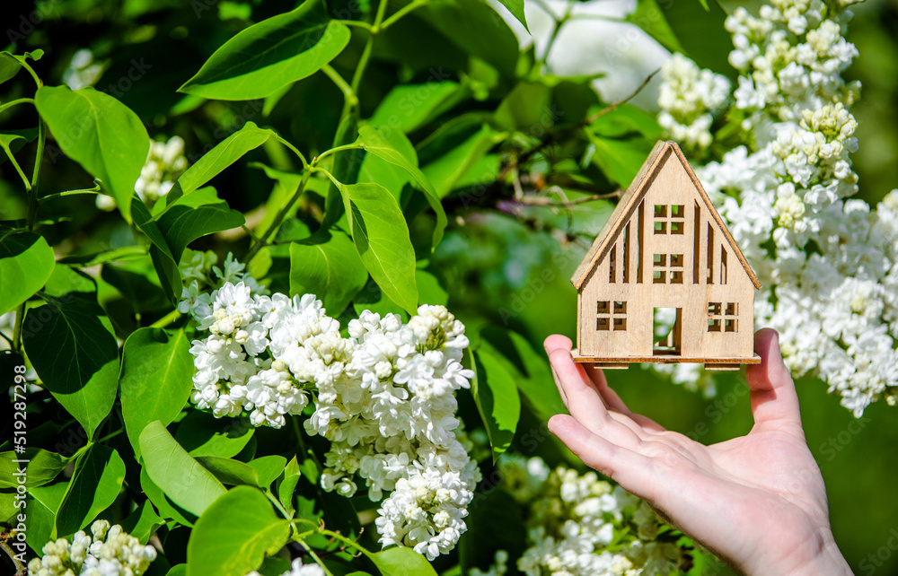 The girl holds the house symbol against the background of blossoming white lilac The girl holds the house symbol against the background of blossoming white lilac