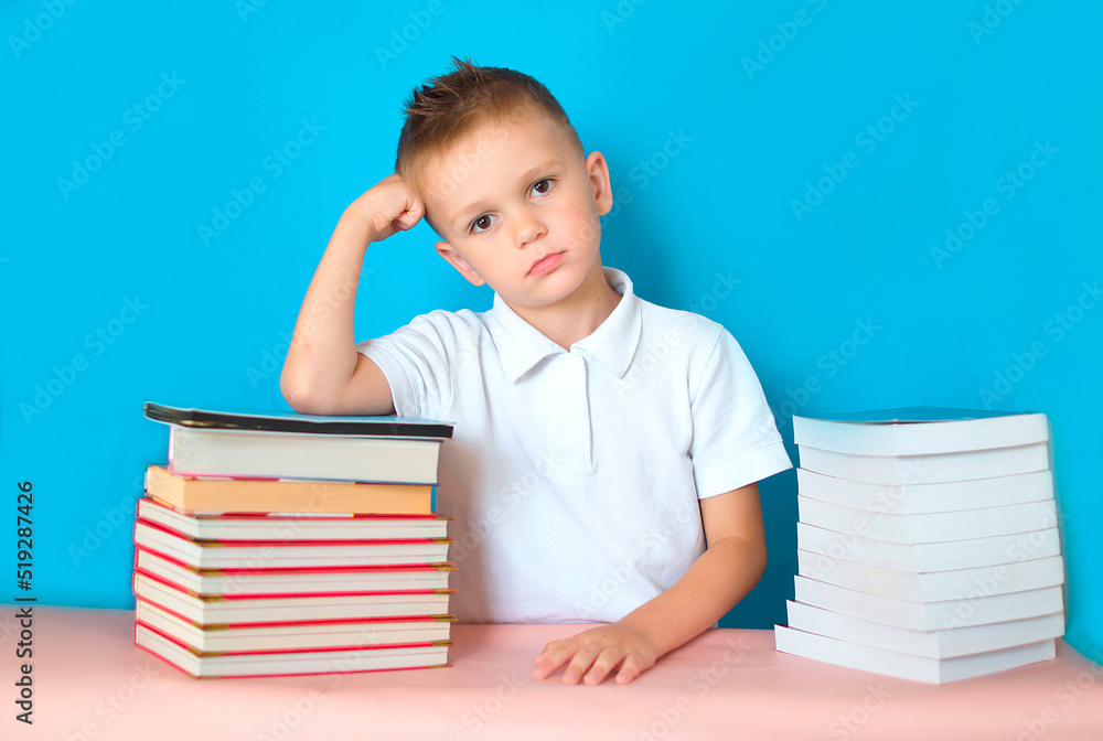 The child is bored while doing homework. A sad, tired, upset boy is sitting at a table with a lot of books. Learning difficulties, the concept of education. Boring homework The child is bored while doing homework. A sad, tired, upset boy is sitting at a table with a lot of books. Learning difficulties, the concept of education. Boring homework