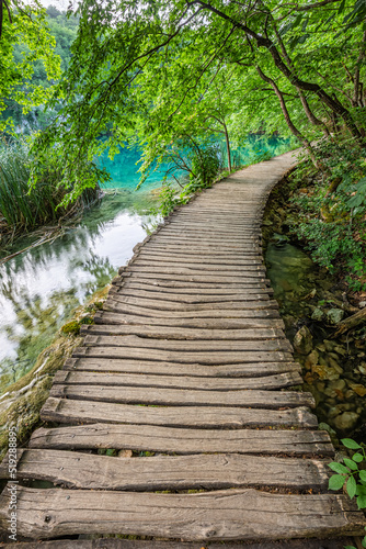 Plitvice  Croatia - Wooden walkway in Plitvice Lakes National Park on a bright summer day with crystal clear turquoise water  small waterfalls and green summer foliage