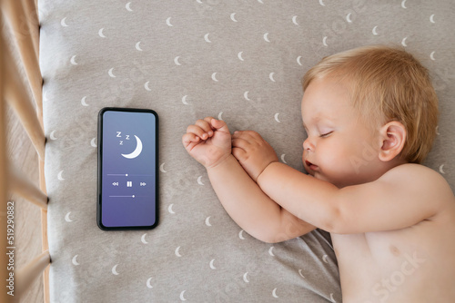 Konstfotografi Upper view of baby napping in his bed next to phone playing lullaby in app for baby sleep with child tracker function and parents remote control settings