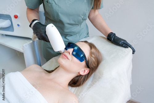Therapist cosmetologist undergoes laser treatment on face young woman in beauty clinic. Facial laser hair. Epilation procedures. Satisfied customer, selective focus.