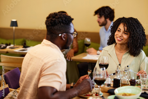 A happy multiracial couple sits in a restaurant, chatting and having dinner together.