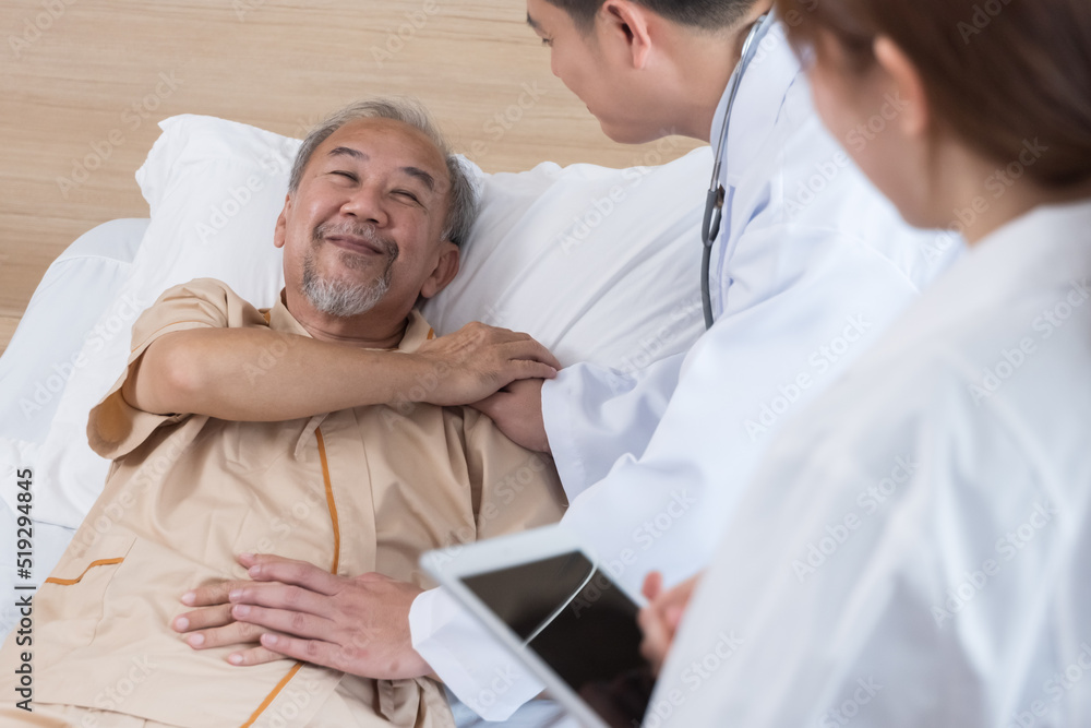 Obraz premium Asian doctor and nurse visit and take care senior man patient in room. Attractive two therapist practitioner explain diagnosis in hospital ward to treatment to elderly older male during appointment.