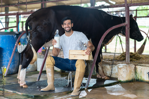 Portrait of Caucasian male dairy farmer hold bottle of milk in cowshed. Handsome young man agricultural smiling and looking at camera after milking cow with feeling proud at livestock farm industry.