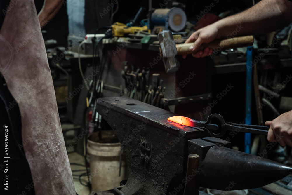 Close up view of heated metal and anvil. Blacksmith in the production process of other metal products handmade in the forge. Metalworker forging metal with a hammer into knife. Metal craft industry. Close up view of heated metal and anvil. Blacksmith in the production process of other metal products handmade in the forge. Metalworker forging metal with a hammer into knife. Metal craft industry.