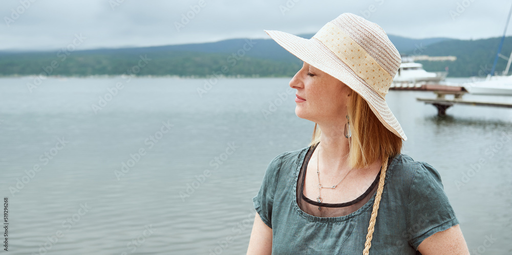Beautiful mature woman in a hat relaxes with her eyes closed resting on the sea in the summer. Copy space for advertising