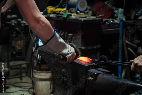 Close up view of heated metal and anvil. Blacksmith in the production process of other metal products handmade in the forge. Metalworker forging metal with a hammer into knife. Metal craft industry.