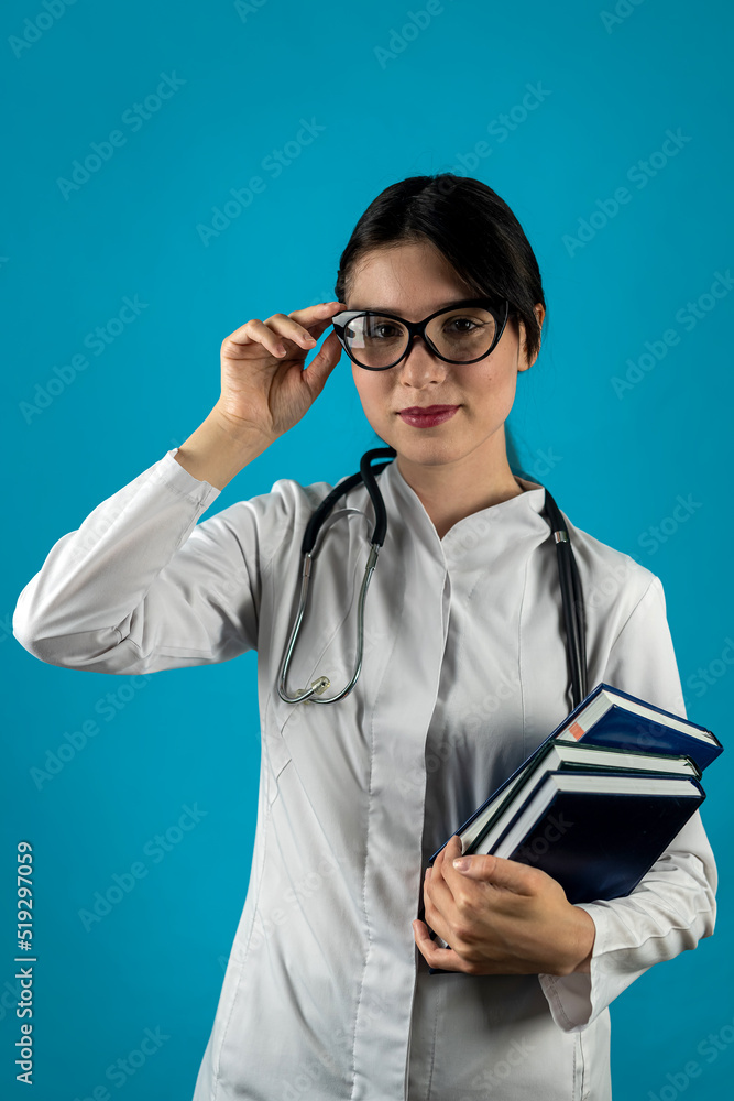 Smiling female doctor with stethoscope and books in hands posing isolated on plain background Smiling female doctor with stethoscope and books in hands posing isolated on plain background
