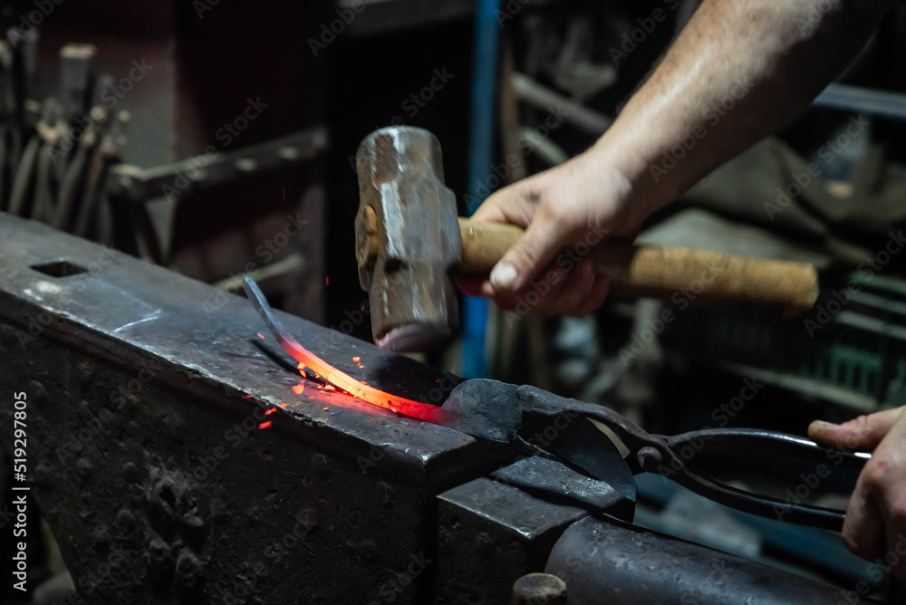 Close up view of heated metal and anvil. Blacksmith in the production process of other metal products handmade in the forge. Metalworker forging metal with a hammer into knife. Metal craft industry. Close up view of heated metal and anvil. Blacksmith in the production process of other metal products handmade in the forge. Metalworker forging metal with a hammer into knife. Metal craft industry.