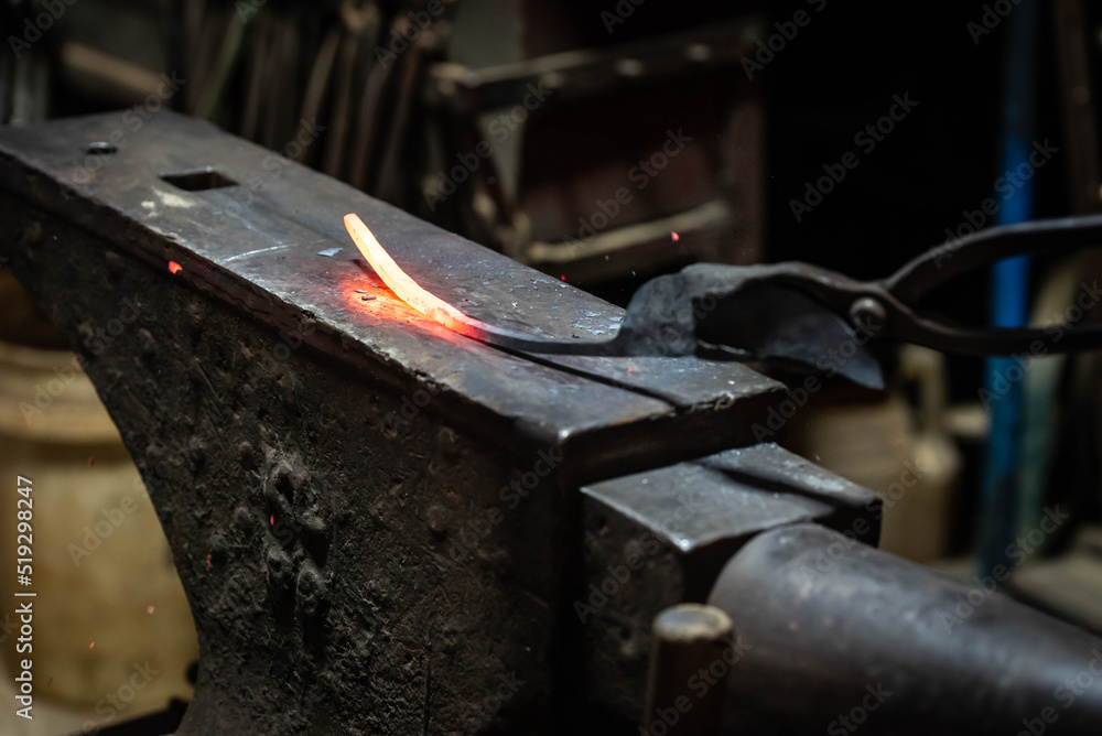 Close up view of heated metal and anvil. Blacksmith in the production process of other metal products handmade in the forge. Metalworker forging metal with a hammer into knife. Metal craft industry. Close up view of heated metal and anvil. Blacksmith in the production process of other metal products handmade in the forge. Metalworker forging metal with a hammer into knife. Metal craft industry.