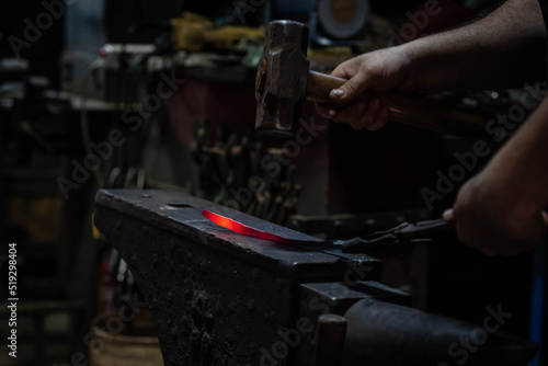 Close up view of heated metal and anvil. Blacksmith in the production process of other metal products handmade in the forge. Metalworker forging metal with a hammer into knife. Metal craft industry.