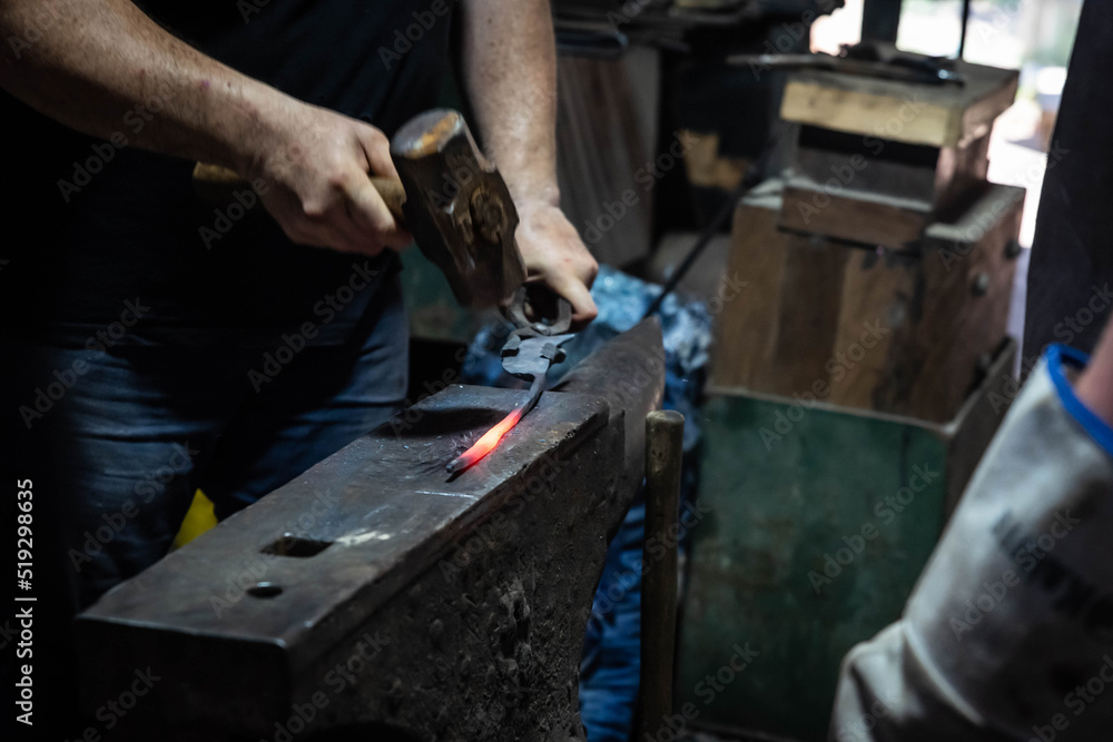 Close up view of heated metal and anvil. Blacksmith in the production process of other metal products handmade in the forge. Metalworker forging metal with a hammer into knife. Metal craft industry. Close up view of heated metal and anvil. Blacksmith in the production process of other metal products handmade in the forge. Metalworker forging metal with a hammer into knife. Metal craft industry.
