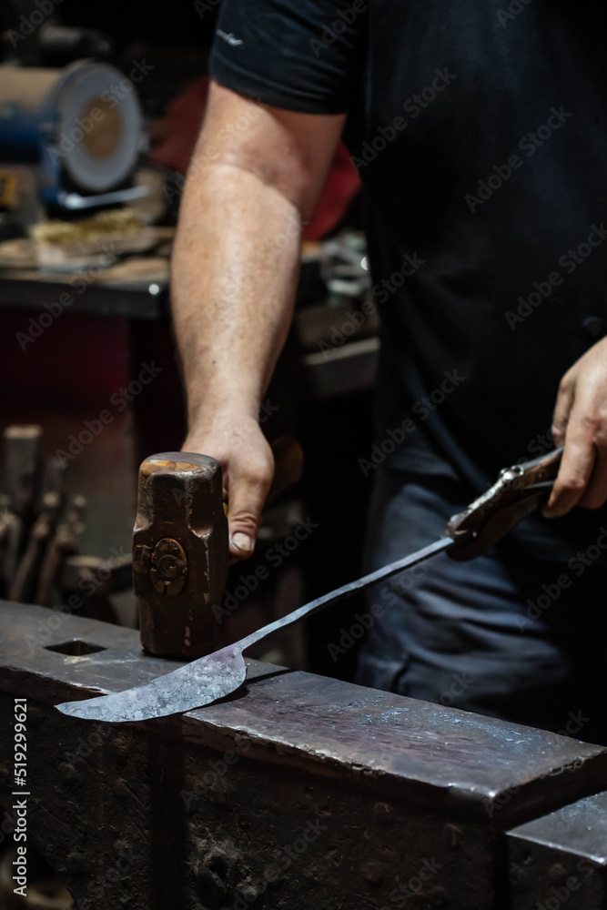 Close up view of heated metal and anvil. Blacksmith in the production process of other metal products handmade in the forge. Metalworker forging metal with a hammer into knife. Metal craft industry. Close up view of heated metal and anvil. Blacksmith in the production process of other metal products handmade in the forge. Metalworker forging metal with a hammer into knife. Metal craft industry.