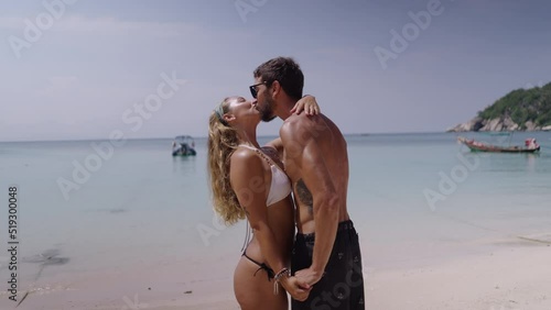 A static shot of affectionately embraced and tenderly kissing, a young couple enjoys a mid summer late afternoon, on a wet sandy beach