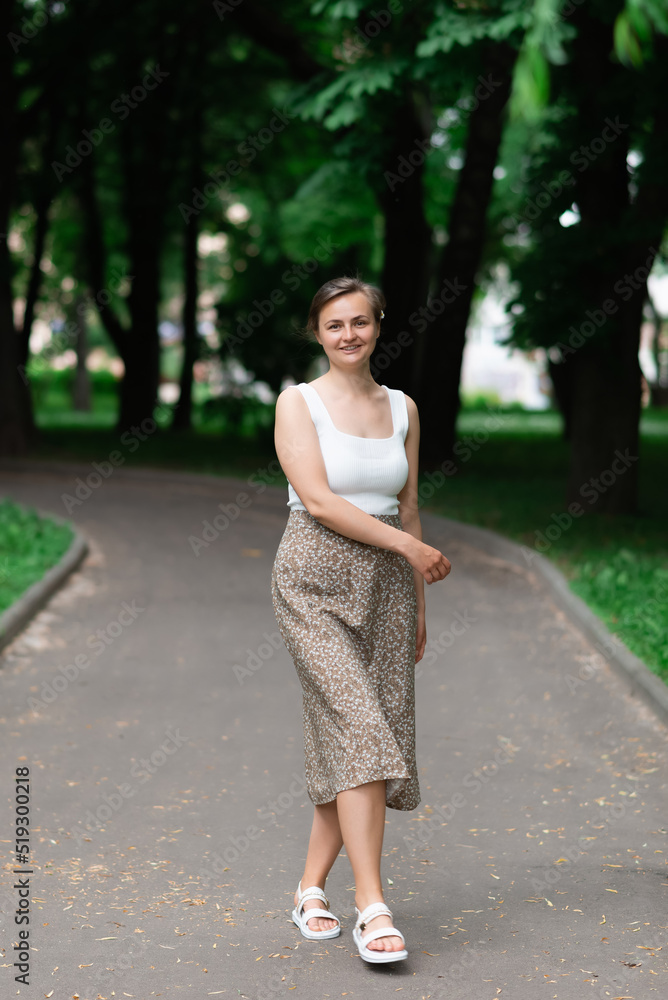 A woman in a white blouse and skirt is walking along the park A woman in a white blouse and skirt is walking along the park