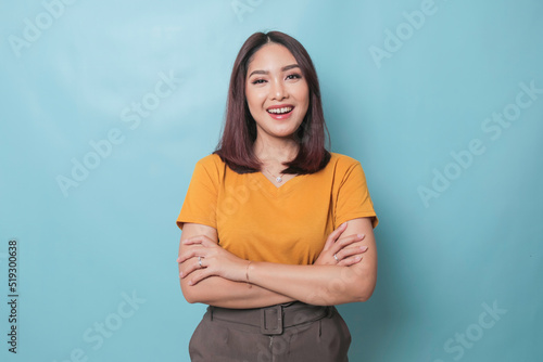 Portrait of a confident smiling girl standing with arms folded and looking at camera isolated over blue background © Reezky