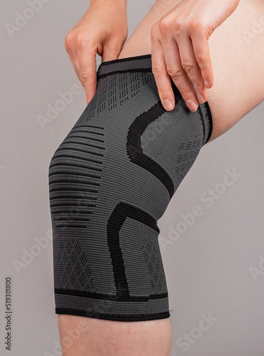 Woman putting on knee brace to support painful leg or heal from injury. Tool used by athlete after trauma for doing sport. Health problems, medical conditions concept. High quality photo