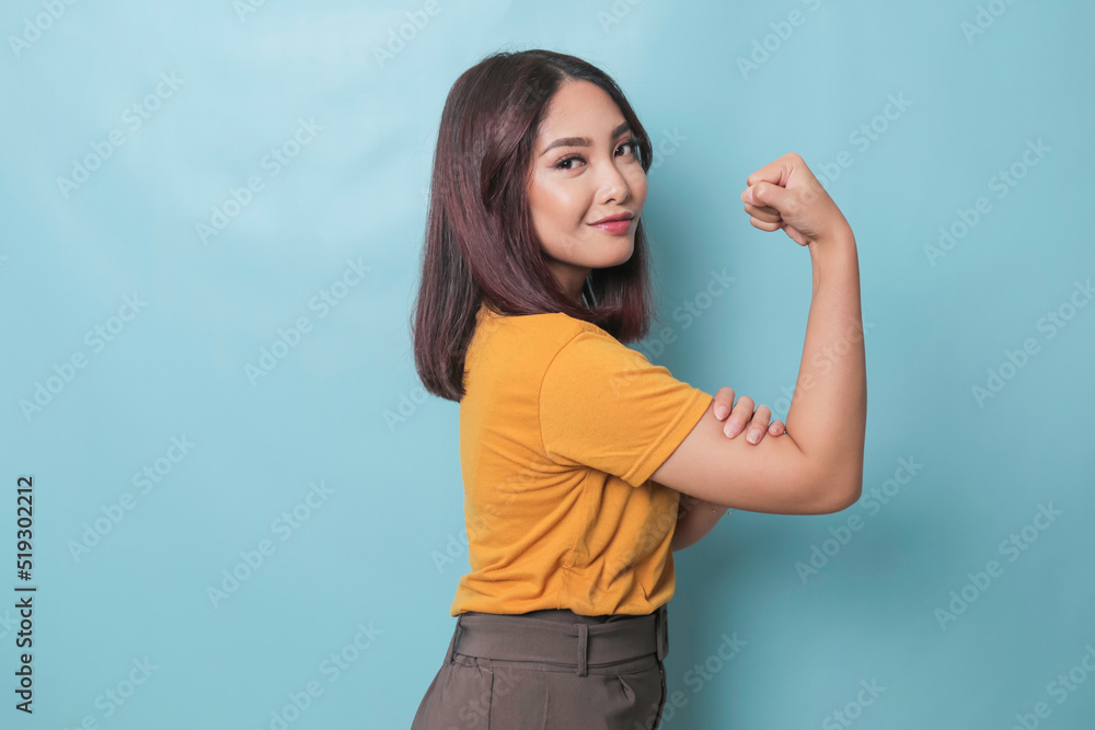 Fototapeta premium Young beautiful girl wearing casual yellow t-shirt standing over isolated blue background showing arms muscles smiling proud. Fitness concept.