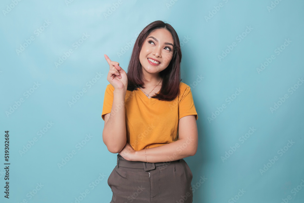 An excited young woman presenting and pointing upwards the copy space, isolated on blue background