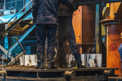 Workers work with molds for smelting iron at steel mill in factory workshop.