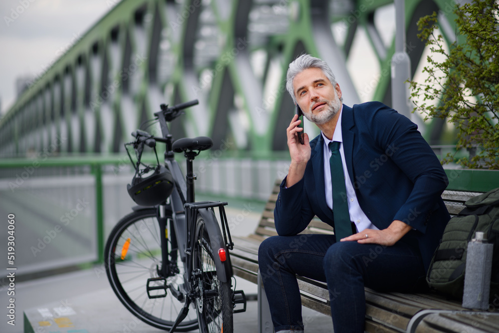 Businessman with bike sitting on bench, using smartphone. Commuting and alternative transport concept