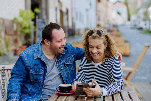 Tableau sur toile Portrait of happy young man with Down syndrome with his mother sitting at cafe outdoors and talking