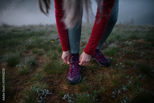 Close-up of senior woman tying her shoelaces before exercise in nature on early morning with fog.