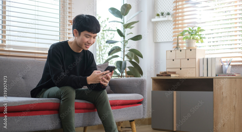 Young Asian man resting on sofa and using smart phone.