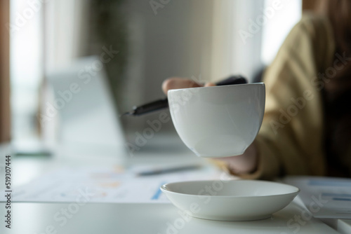 Close up view of businesswoman hand holding coffee cup over white office desk near.