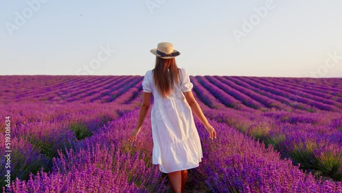 Young woman in white dress walking through a lavender field on sunset