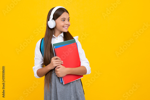 Teenager school girl wearing headphones reading a book over isolated yellow background. Happy girl face, positive and smiling emotions.