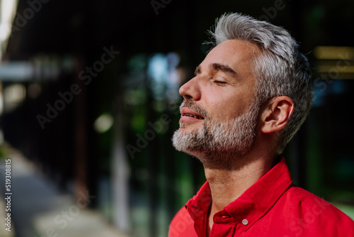 Cheerful mature businessman keeping eyes closed and taking a deep breath while standing outside during a break from work. photo