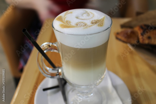 A glass cup of aromatic cappuccino coffee with foam and a pattern stands on a white saucer