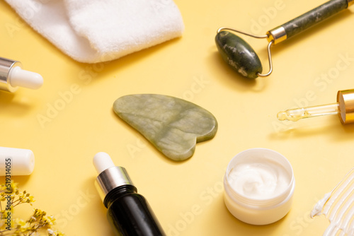 Serum and moisturizing cosmetic cream with facial massager on colored background