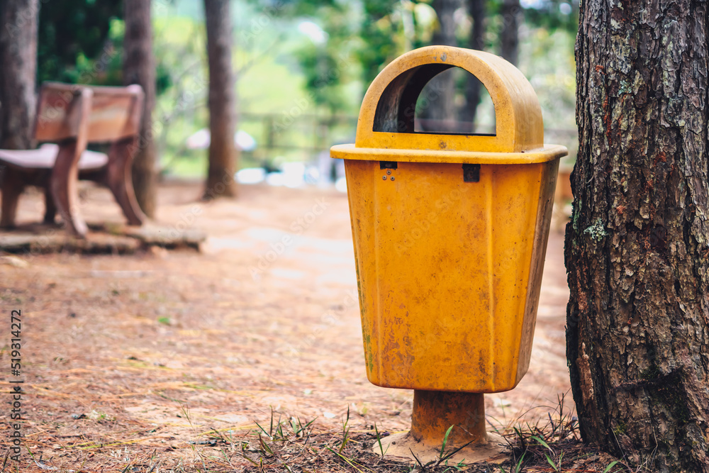 Yellow orange garbage bin in forest park helps to save no public trash on side ground of path. Concept Infection control, disposal of waste, outdoor open air can, conservation of nature, clean planet Yellow orange garbage bin in forest park helps to save no public trash on side ground of path. Concept Infection control, disposal of waste, outdoor open air can, conservation of nature, clean planet