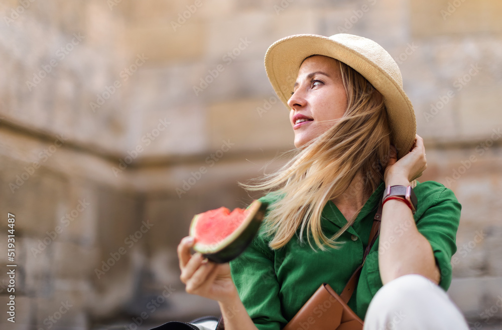 Young woman traveller eating watermelon in street during hot sunny day, summer vacation trip concept.