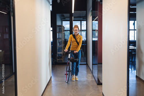 Mid adult caucasian businesswoman with bicycle in corridor of creative office