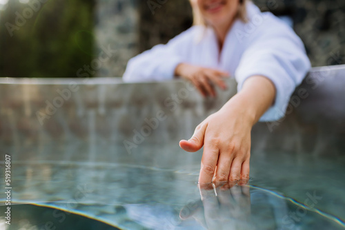 Fotografi Unrecognizable woman in towel touching water, checking temperature, ready for home spa procedure in hot tub outdoors