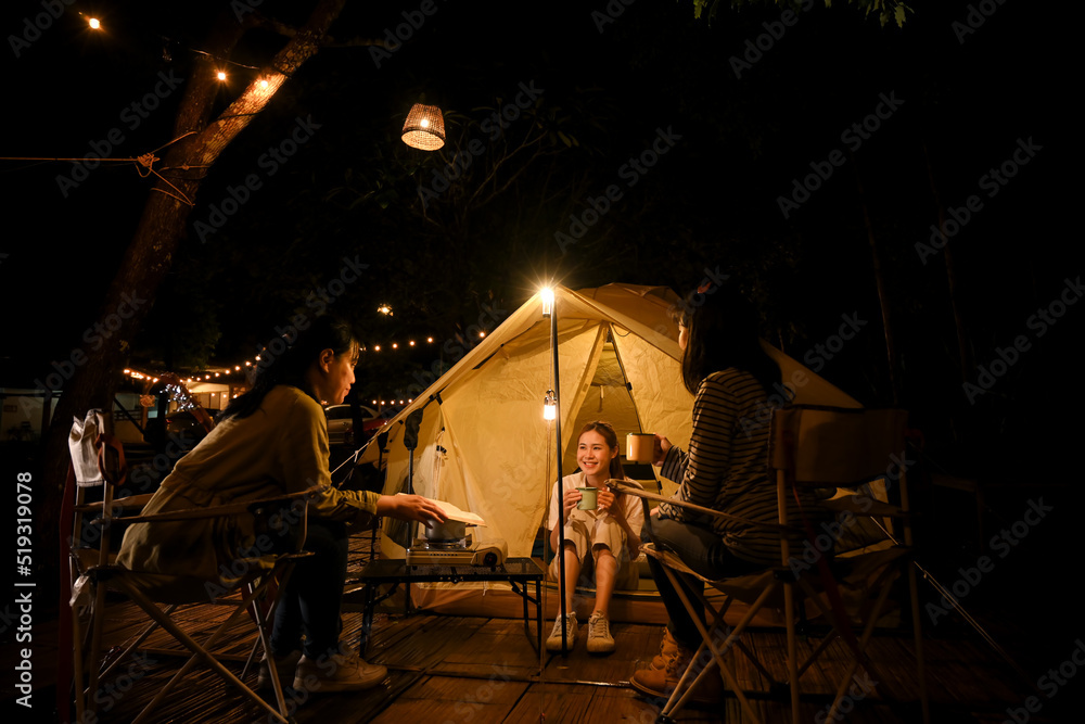 A group of an Asian female teenagers enjoy camping and looking at the stars at night together - obrazy, fototapety, plakaty 